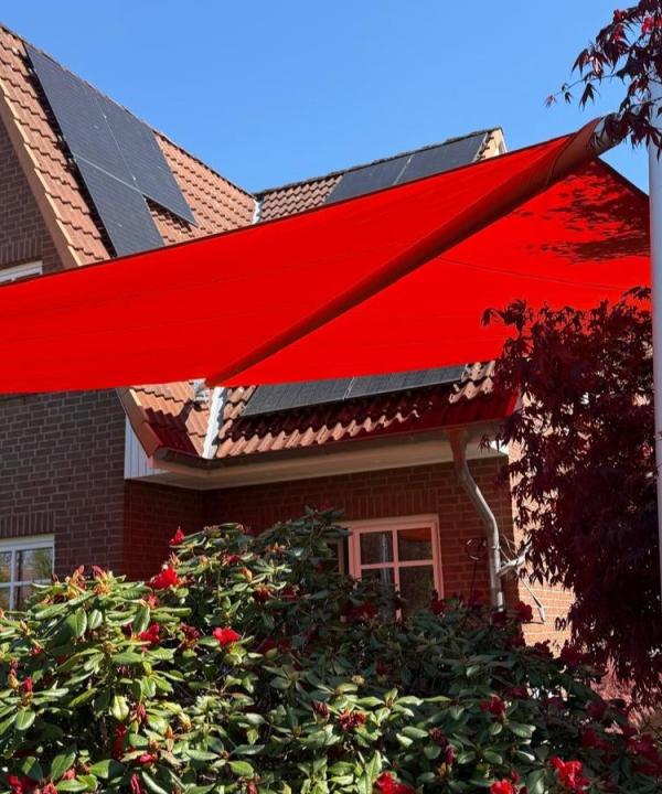 rotes sonnensegel in blühendem Garten vor einem Einfamilienhaus mit backsteinfassade in hmaburg-schnelsen von zschimmer