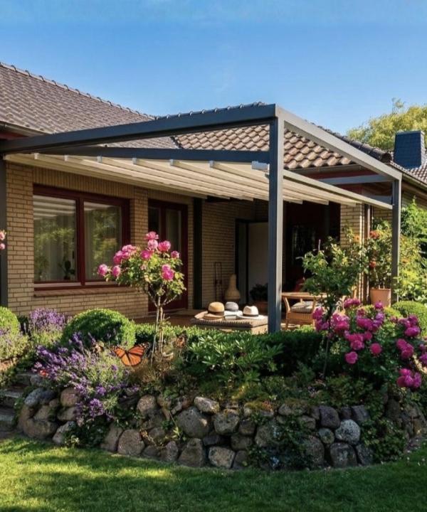 Ausgefahrene, weiße Pergola Markise Sunrain Q mit abgesenkten Markisentuch überspannt die Terrasse eines Einfamilienhaus