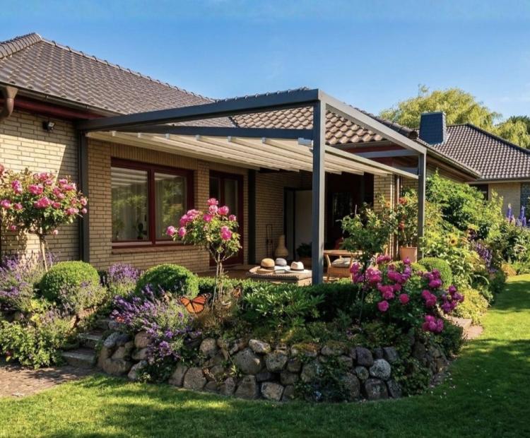 Ausgefahrene, weiße Pergola Markise Sunrain Q mit abgesenkten Markisentuch überspannt die Terrasse eines Einfamilienhaus